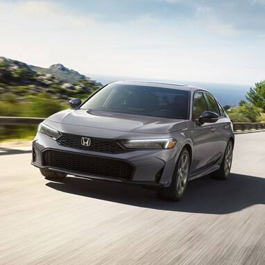 2027 Honda Civic Sedan Sport Touring Hybrid in Urban Gray Pearl front three-quarter view driving on a road (Compact Sedan)